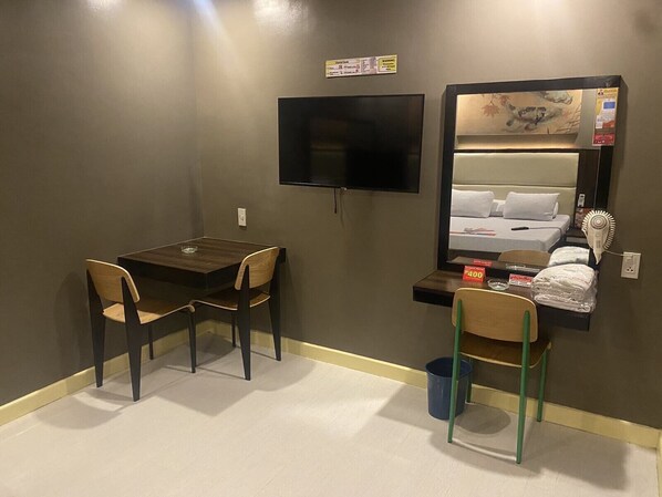 Habitación de hotel con escritorio, dos sillas, televisor, cama con espejo y secador de pelo.