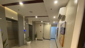 Un pasillo moderno con piso pulido, un ascensor, una planta en maceta y una puerta con un cartel.