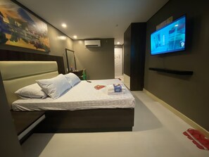 Un hotel moderno con una cama grande, un televisor de pantalla plana montado en la pared y un cuadro sobre la cama.