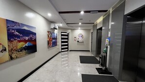 Un pasillo con piso de baldosas, un felpudo negro en la entrada, un equipo de aire acondicionado instalado en la pared y una puerta con un estampado a rayas blancas y negras.