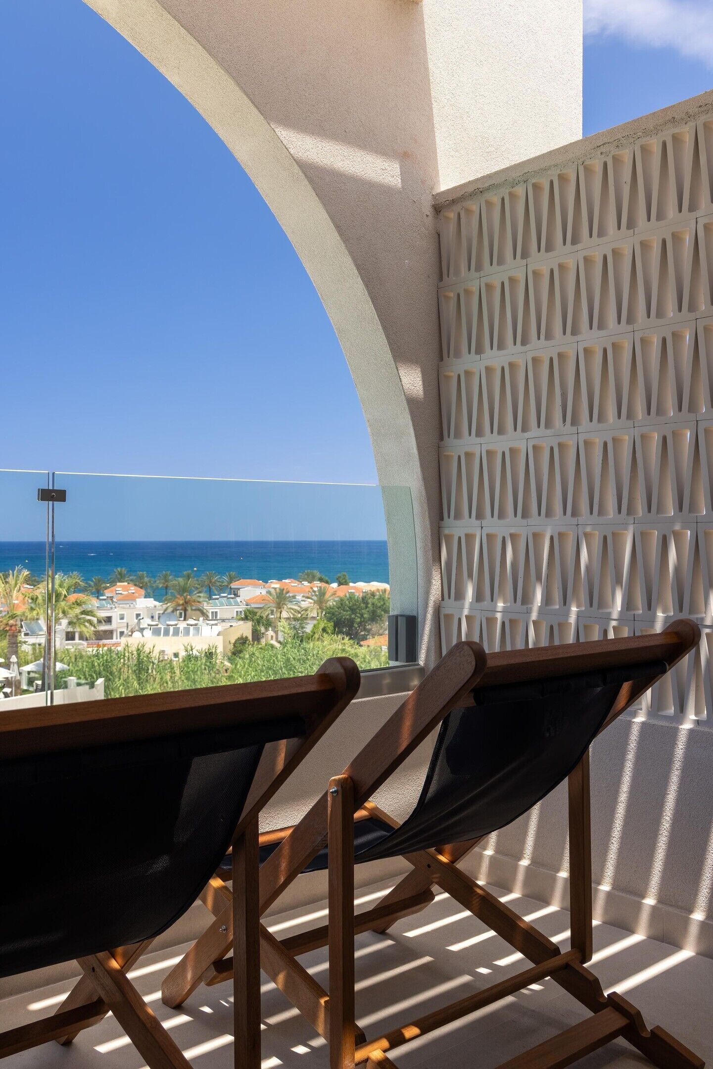 A balcony with a view of the sea and buildings, a wooden chair, and a white acoustic panel.