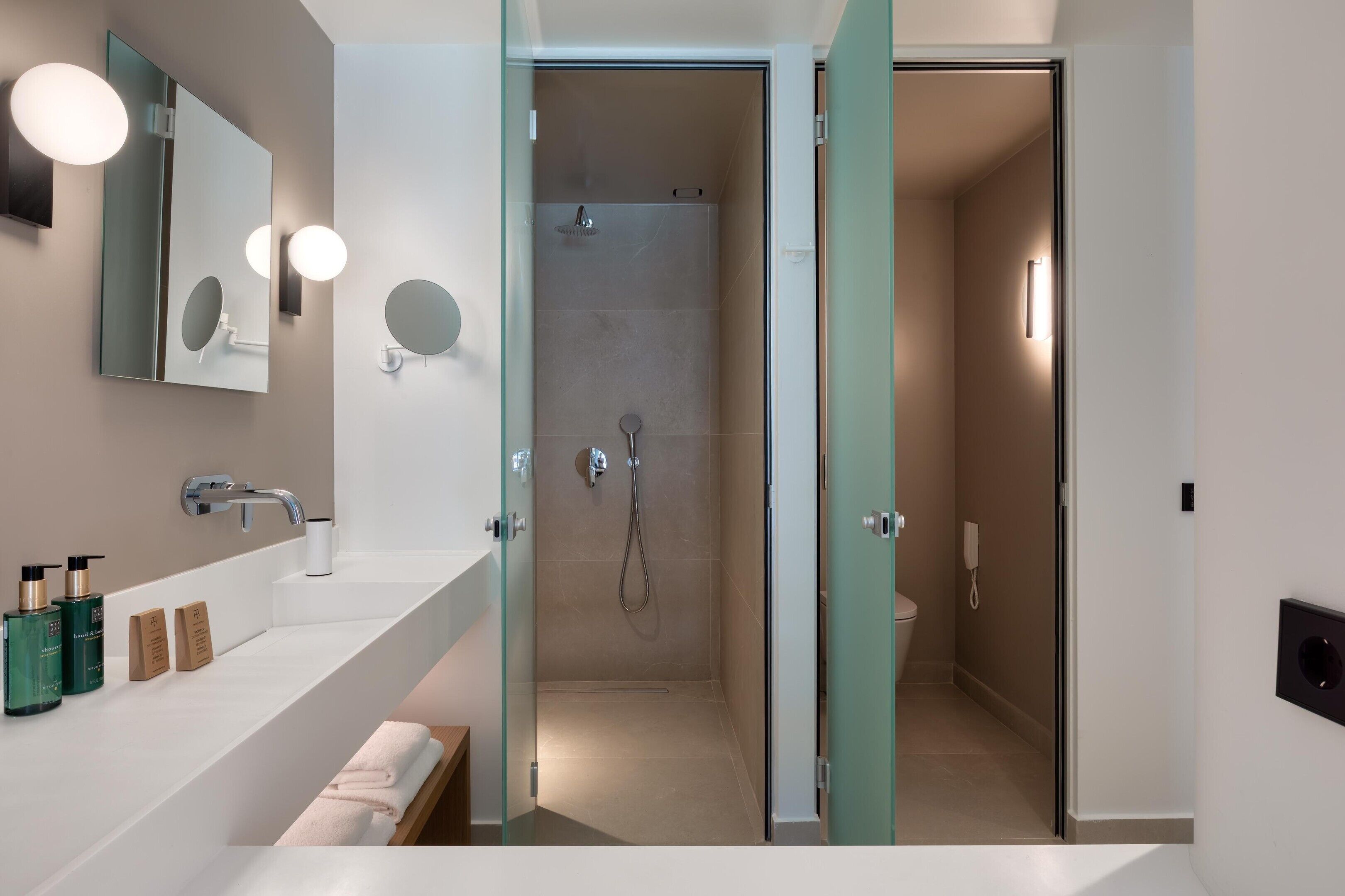 A modern bathroom with a glass shower enclosure, a white sink with a mirror, and a towel rack.