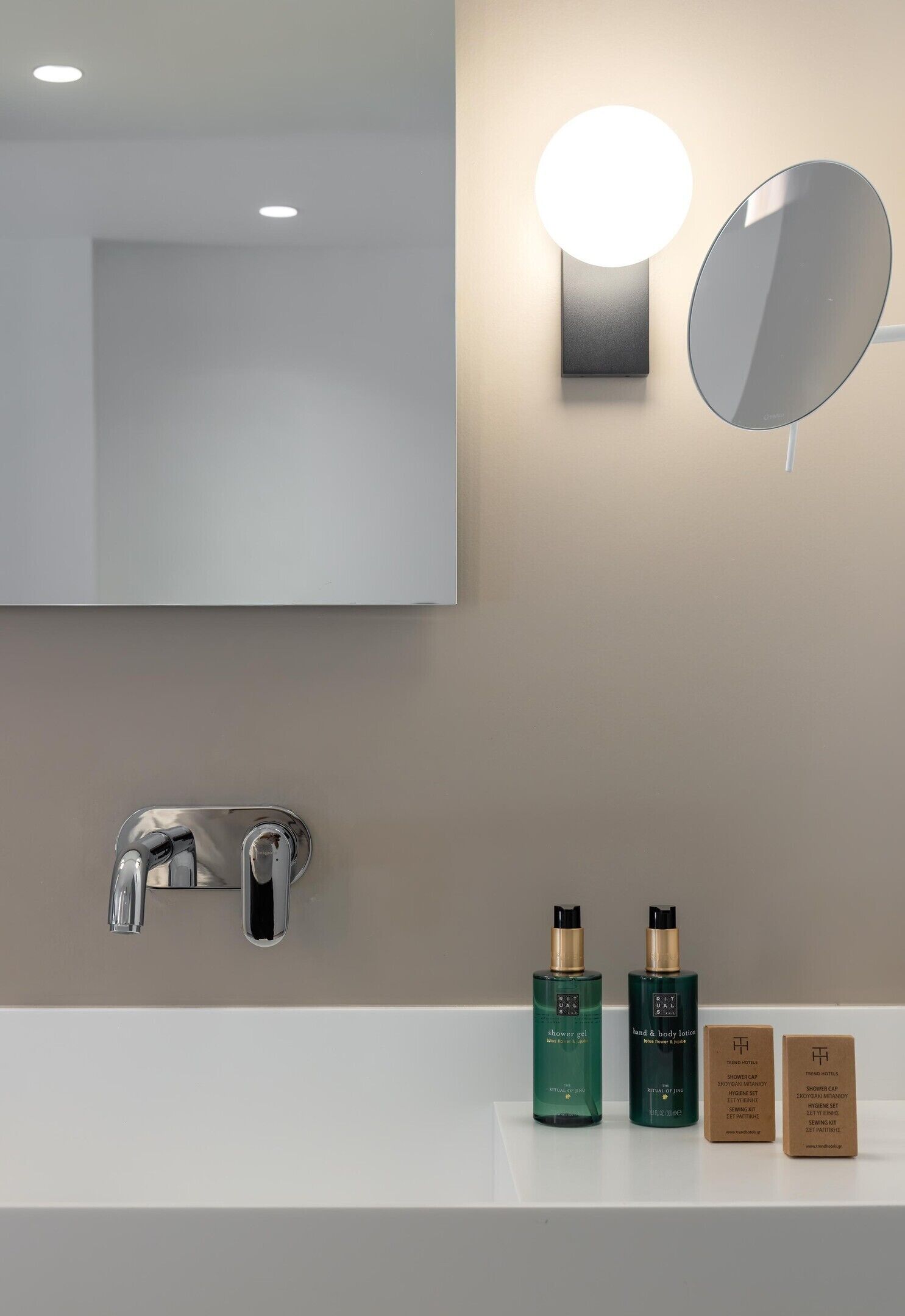 A bathroom with a mirror, wall-mounted light, and a sink with two bottles and two boxes.