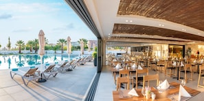A poolside area with lounge chairs and umbrellas, a dining area with tables and chairs, and a view of the pool. - Dore Hotel (Chania)