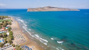 A beach with a long stretch of sand, umbrellas, and a few people. - Dore Hotel (Chania)