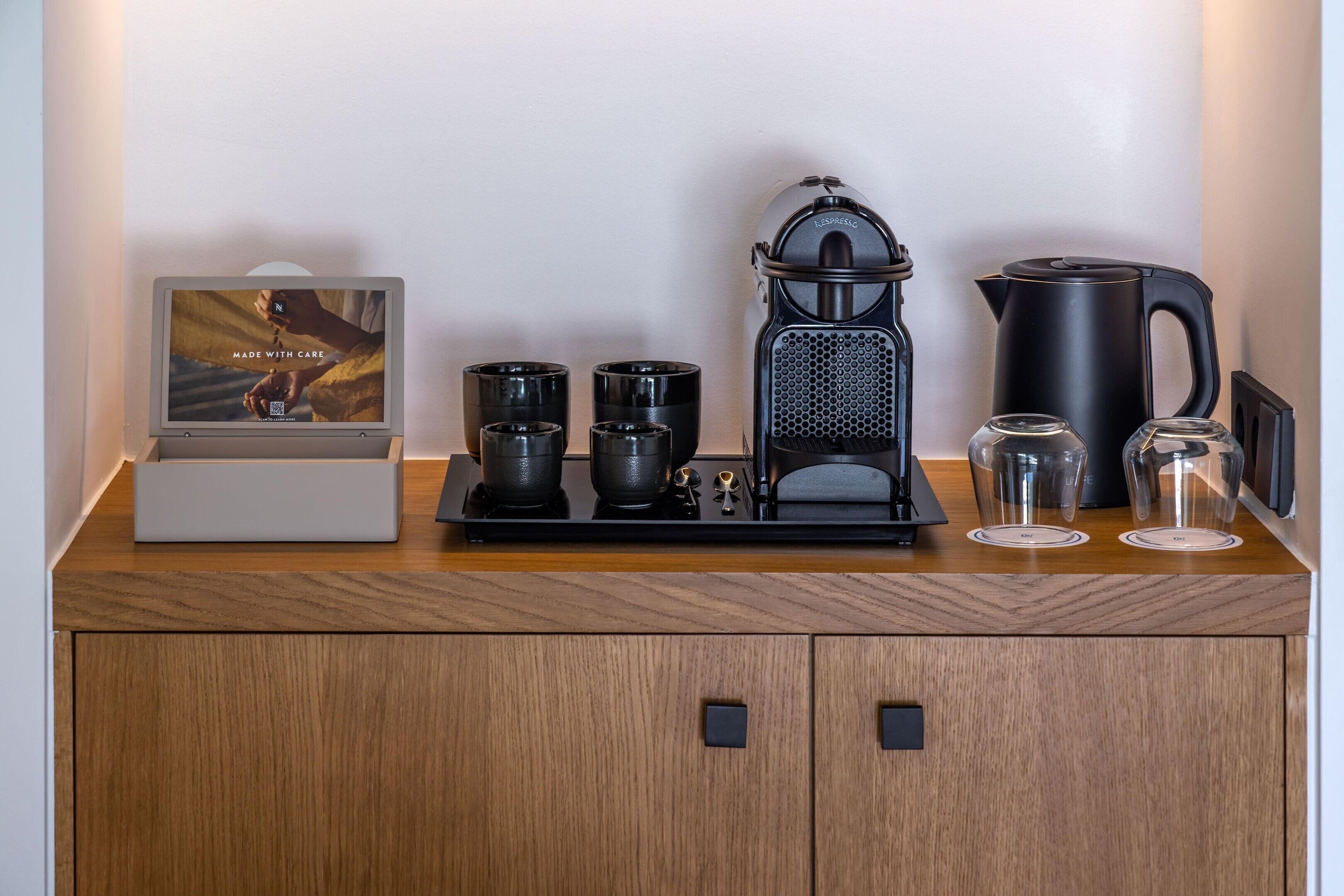 A coffee station with a coffee maker, cups, a kettle, and a small display.