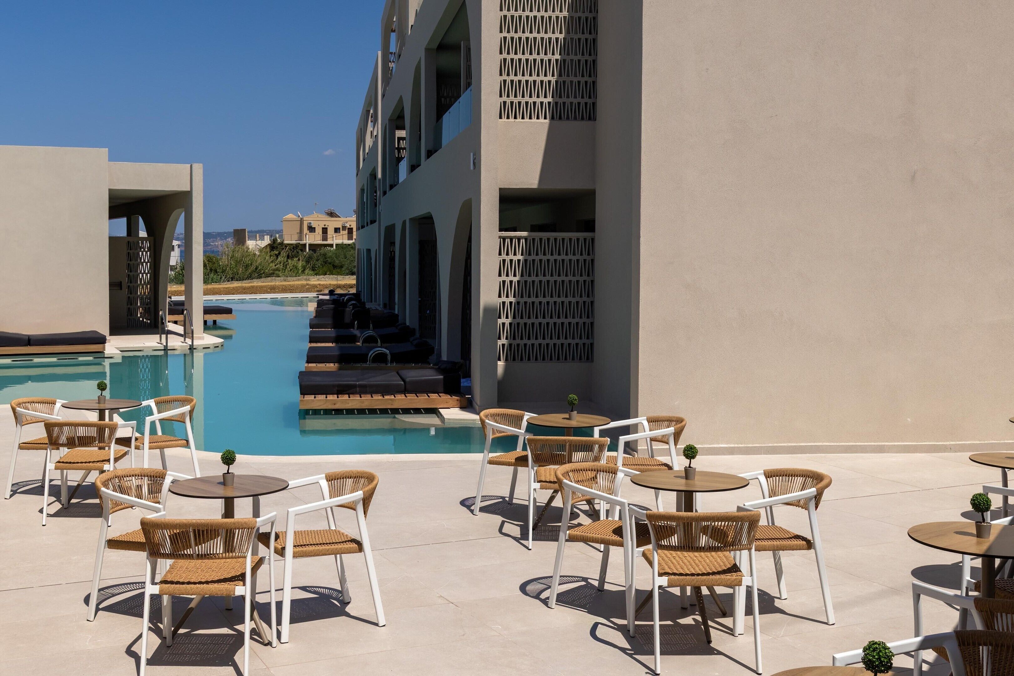 A poolside area with lounge chairs and tables, a pool, and a building with a geometric facade.