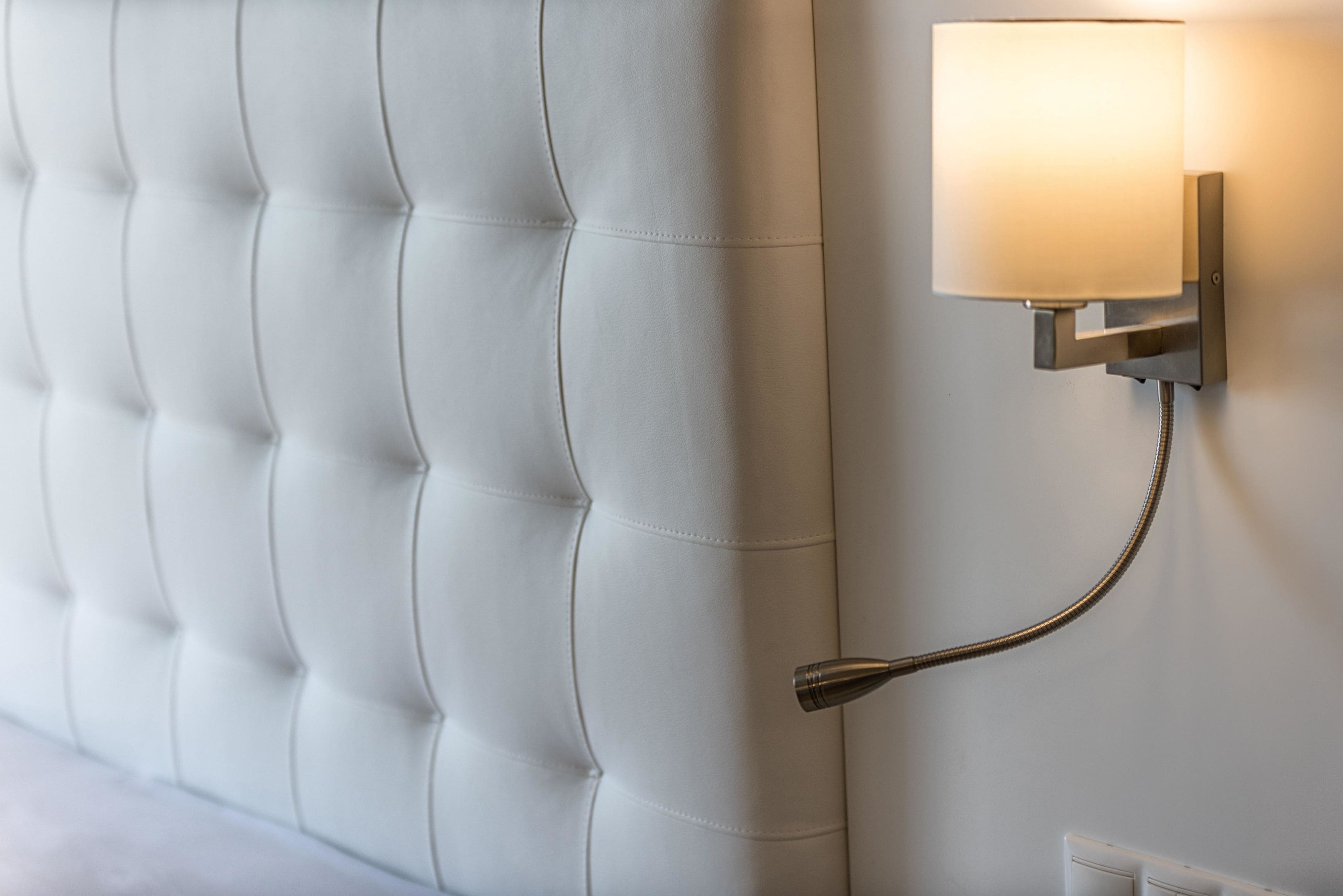 A wall-mounted light fixture with a flexible arm, attached to a wall with a tufted headboard.