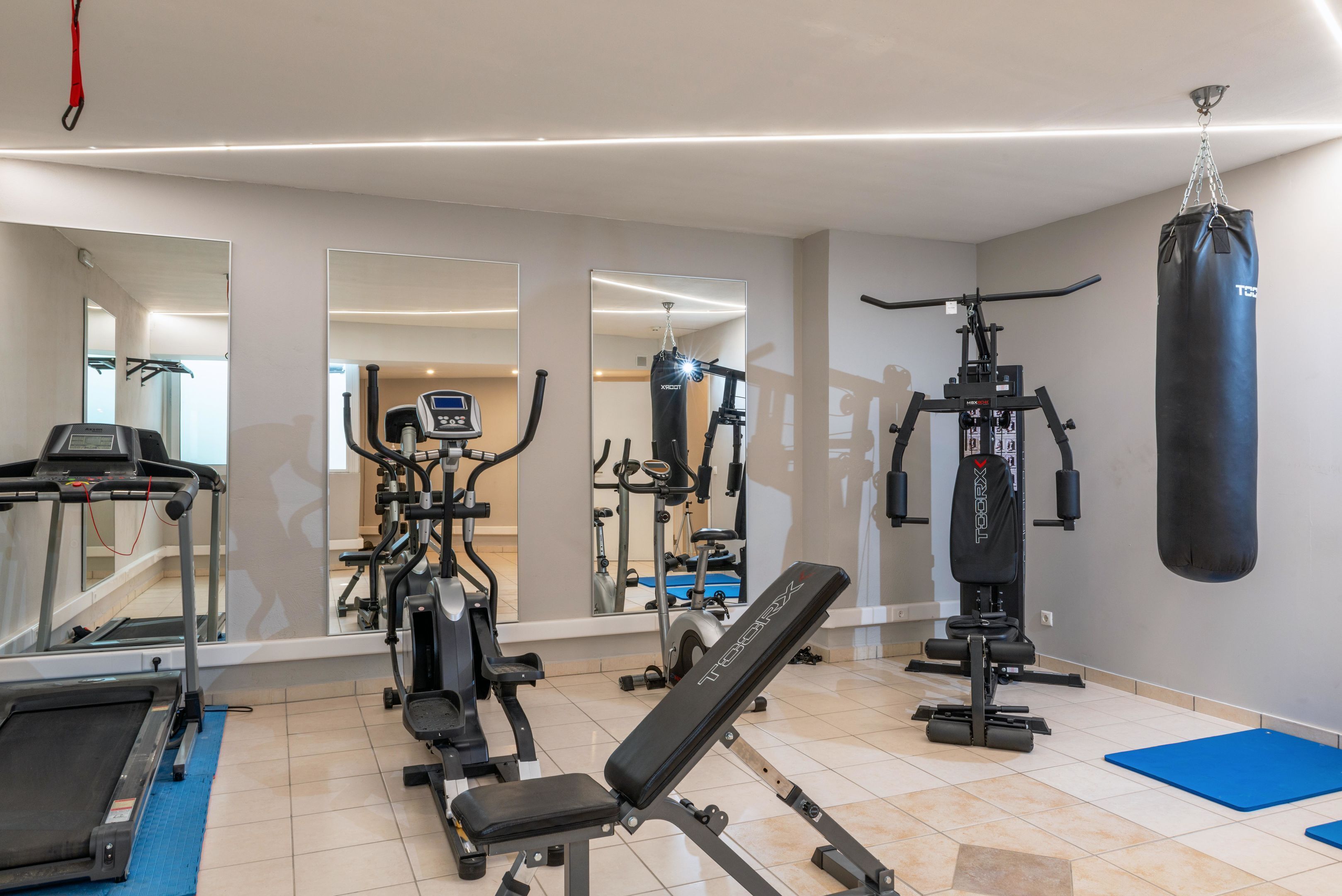 Une salle de sport équipée de matériel d’exercice, d’un sac de frappe et d’un banc.