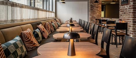 A modern restaurant with round tables, cushioned seating, pendant lighting, and brick walls.
