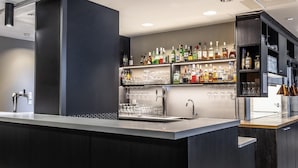 A modern bar area with a dark wood finish, stainless steel bar counter, and shelves stocked with various liquor bottles and glasses. - Scandic Postitalo (Tampere)