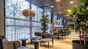 A modern interior with large windows, wicker pendant lights, and a variety of seating arrangements. - Scandic Postitalo (Tampere)