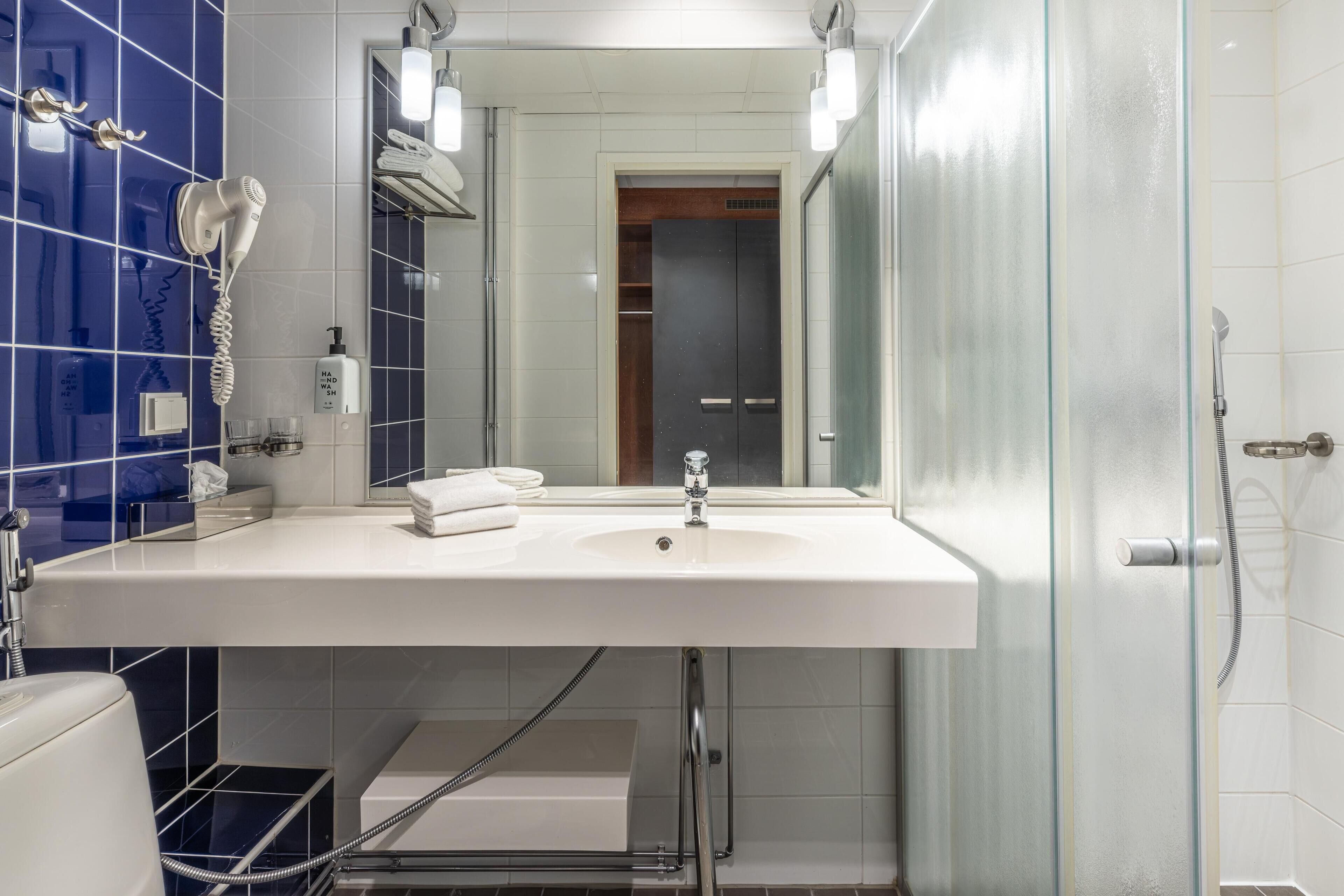 Un bagno con un lavandino bianco, un asciugacapelli, uno specchio e una cabina doccia in vetro.