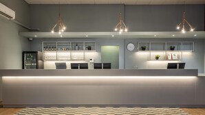A modern reception area with a reception desk, a refrigerator, and shelves with items. - Scandic Postitalo (Tampere)