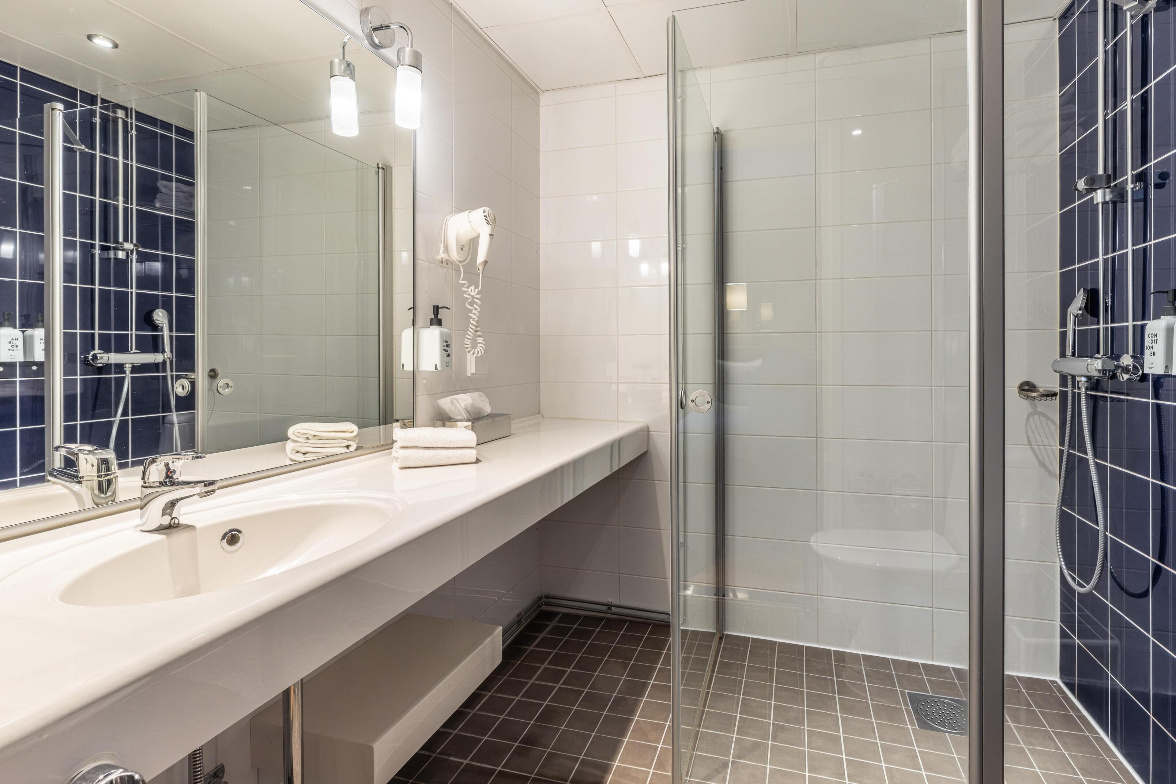 A modern bathroom with a large mirror, a white sink, a glass shower enclosure, and blue-tiled walls.