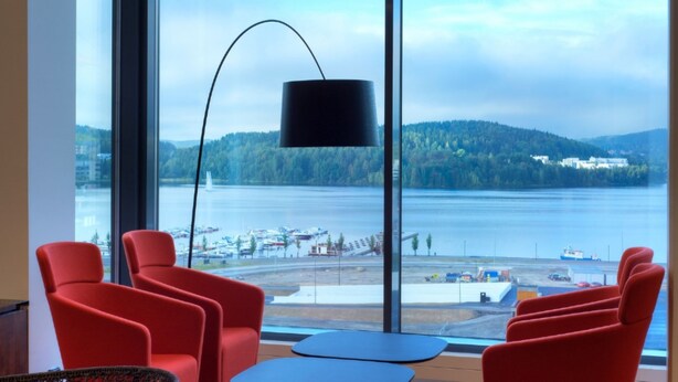 Een moderne kamer met grote ramen, rode stoelen, een blauwe tafel en een vloerlamp in het zwart.