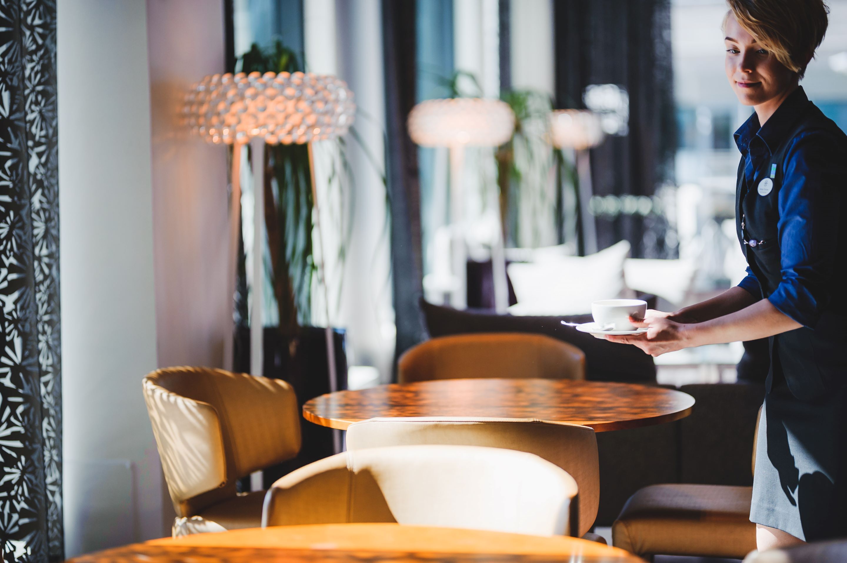 Una persona servint cafè en un café modern amb taules rodones i seients còmodes.