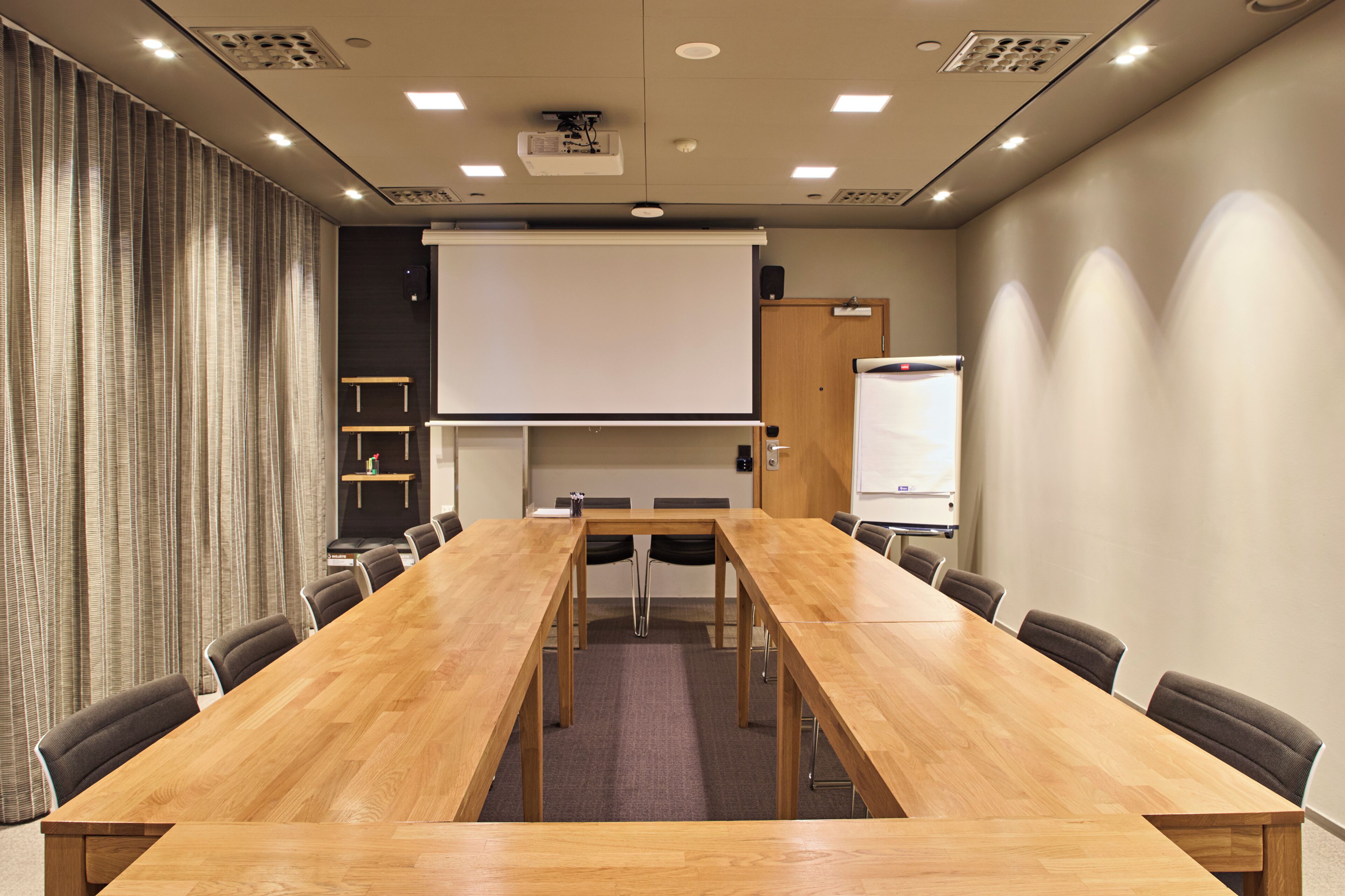 Une salle de conférence équipée d’une longue table en bois, de chaises, d’un écran de projection et d’un tableau blanc.