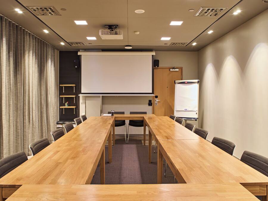 Une salle de conférence équipée d’une longue table en bois, de chaises, d’un écran de projection et d’un tableau blanc.