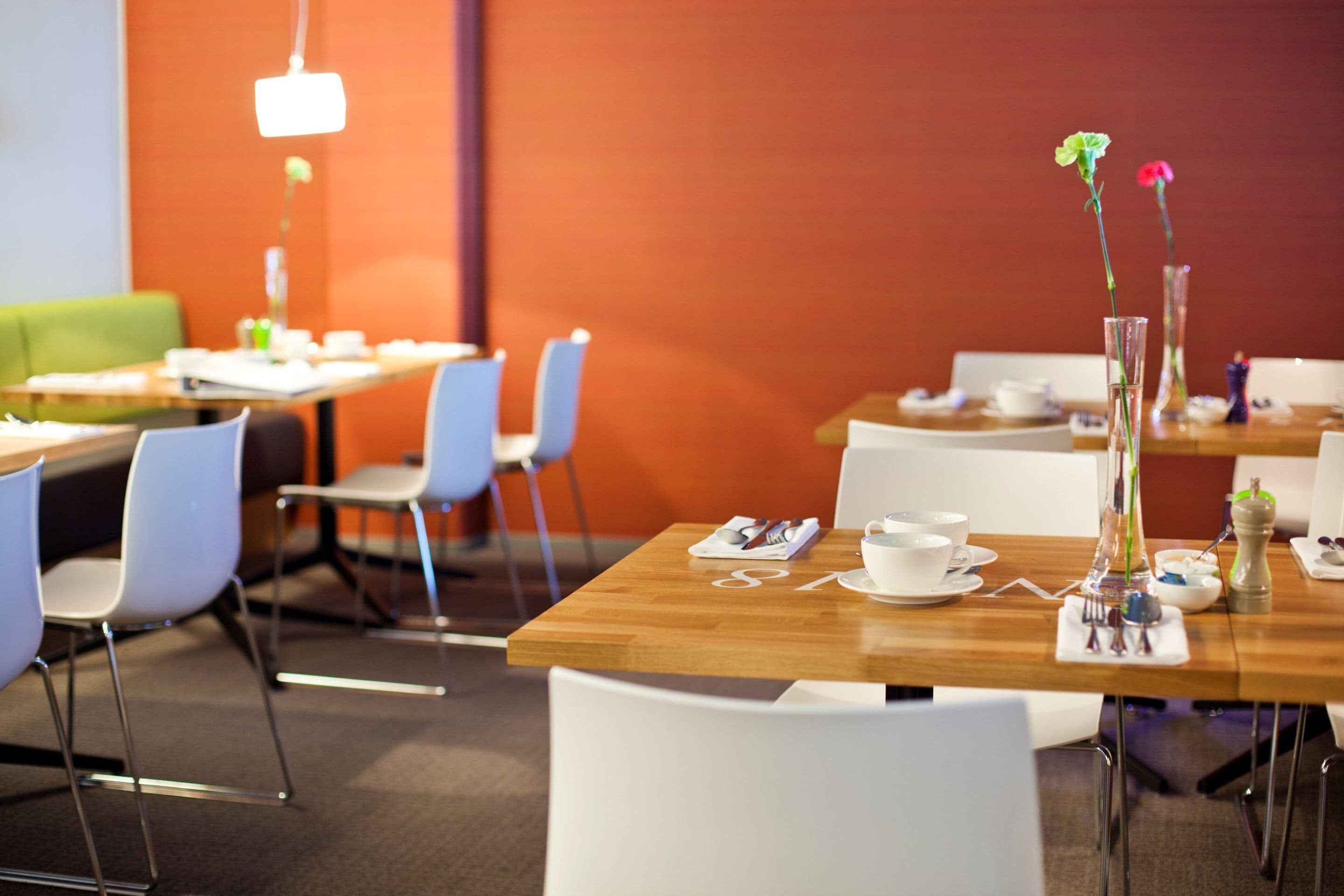 A dining area with tables set for breakfast, white chairs, and a vase with flowers on one table.