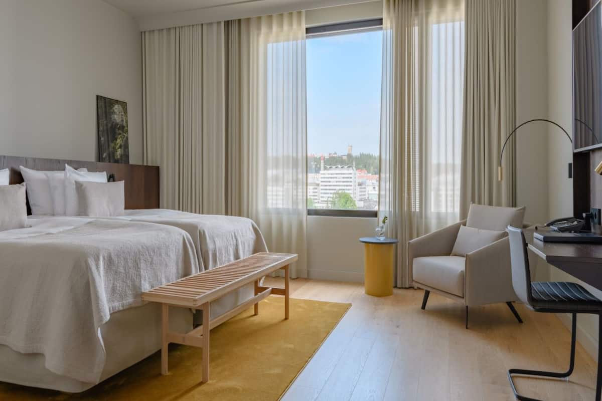 Ein Hotelzimmer mit einem großen Bett, einem Schreibtisch, einem Stuhl und Blick auf die Stadt durch das Fenster.