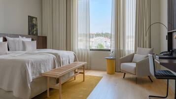 A hotel room with a large bed, a desk, a chair, and a view of the city through the window.
