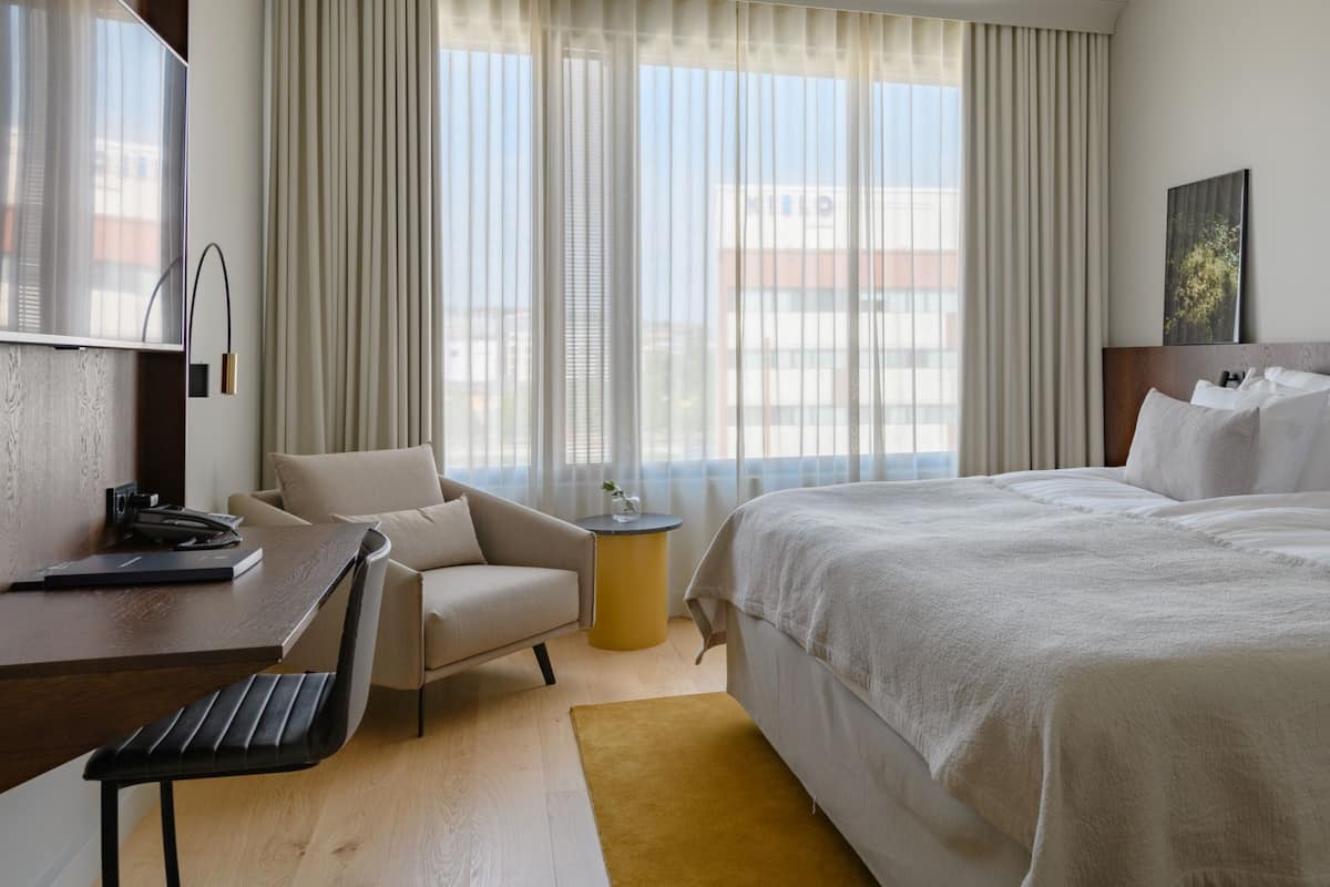 Ein Hotelzimmer mit Bett, Schreibtisch mit Telefon, Stuhl und kleinem Tisch mit Vase.