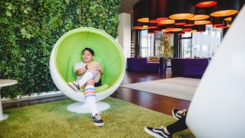 Guests can sit in the egg-shaped chair on the carpeted floor, surrounded by lush foliage and a purple seating area.