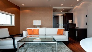 Un salon moderne avec un canapé blanc, des coussins orange, une table basse en verre et une lampe blanche.