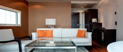 Un salon moderne avec un canapé blanc, des coussins orange, une table basse en verre et une lampe blanche.
