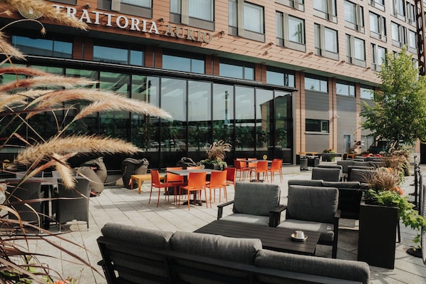 An outdoor seating area with tables and chairs, a building with a sign reading 'TRATTORIA AKIO', and large windows. - Solo Sokos Hotel Paviljonki (Jyväskylä)
