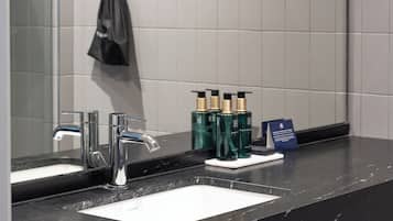 Un baño con encimera de mármol negro, lavamanos blanco, grifo cromado y espejo que refleja el ambiente.