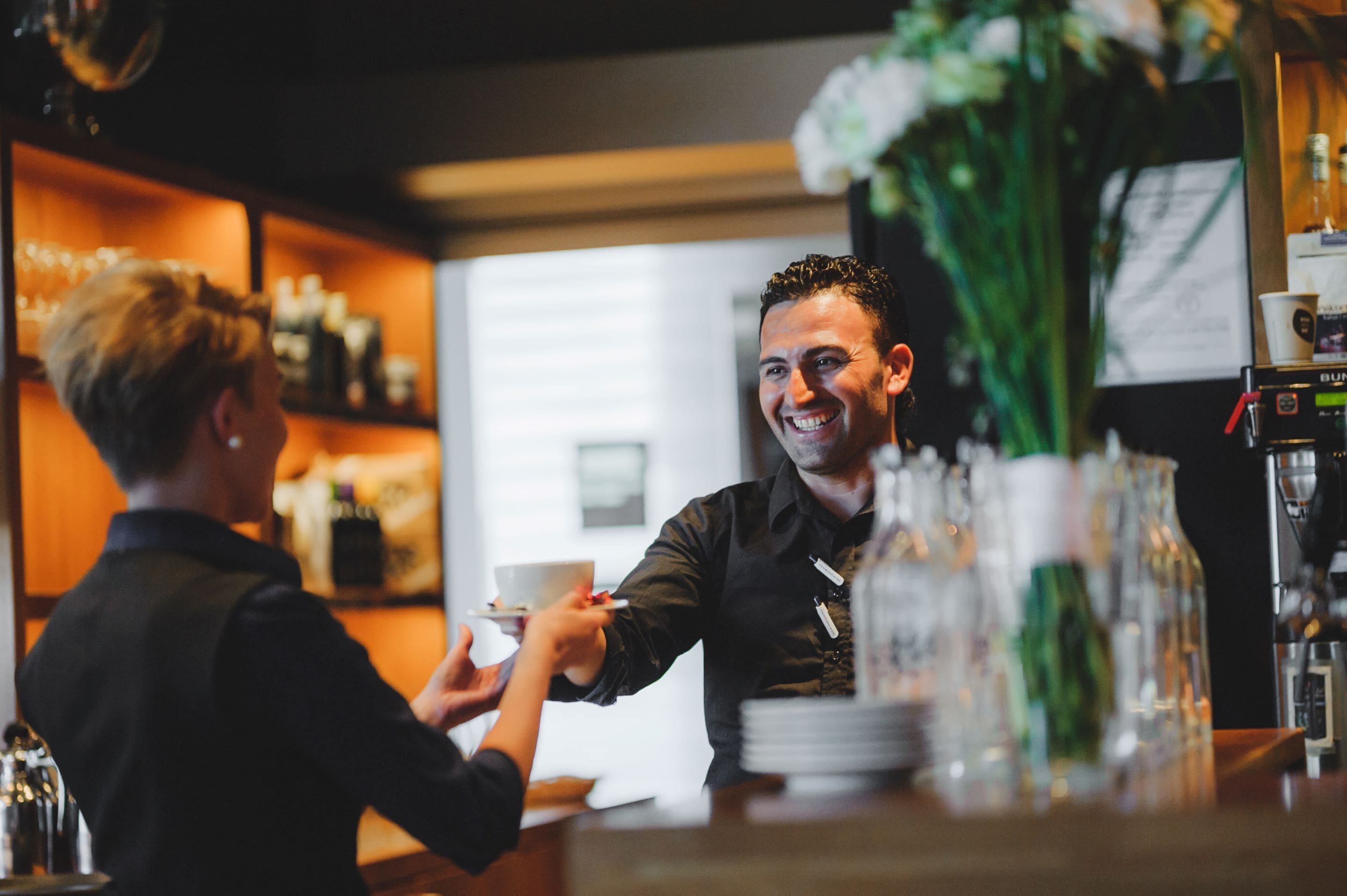 Un espace bar avec un comptoir, une machine à café et un vase rempli de fleurs.