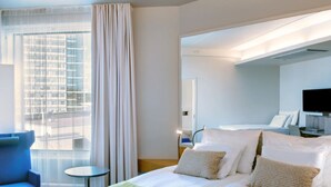 Een hotelkamer met een bed, bureau, stoel, televisie en een raam met gordijnen.