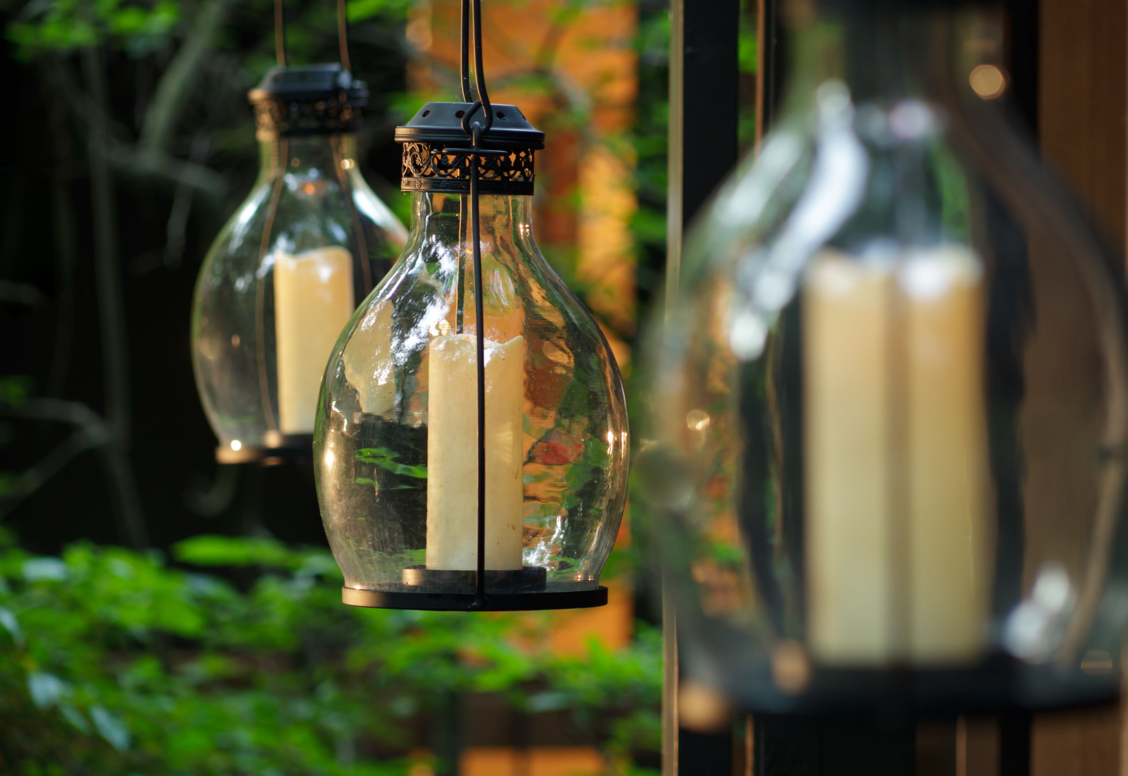 Three hanging glass lanterns with candles inside, suspended by black metal fixtures.