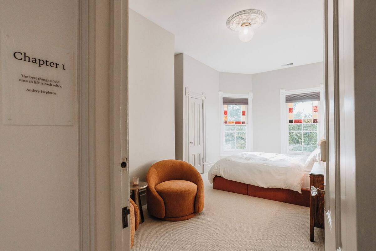 A bedroom with a large bed, a round orange chair, and a white ceiling light.