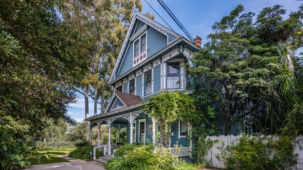 A two-story house with a porch, surrounded by lush greenery and a white picket fence. - Kaleidoscope Inn & Gardens (Nipomo)