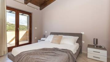 A bedroom with a bed, a nightstand, a window with curtains, and a view of the outdoors.