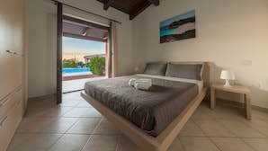 Une chambre avec un lit, une table de chevet, un tableau et une vue sur une piscine et la verdure.