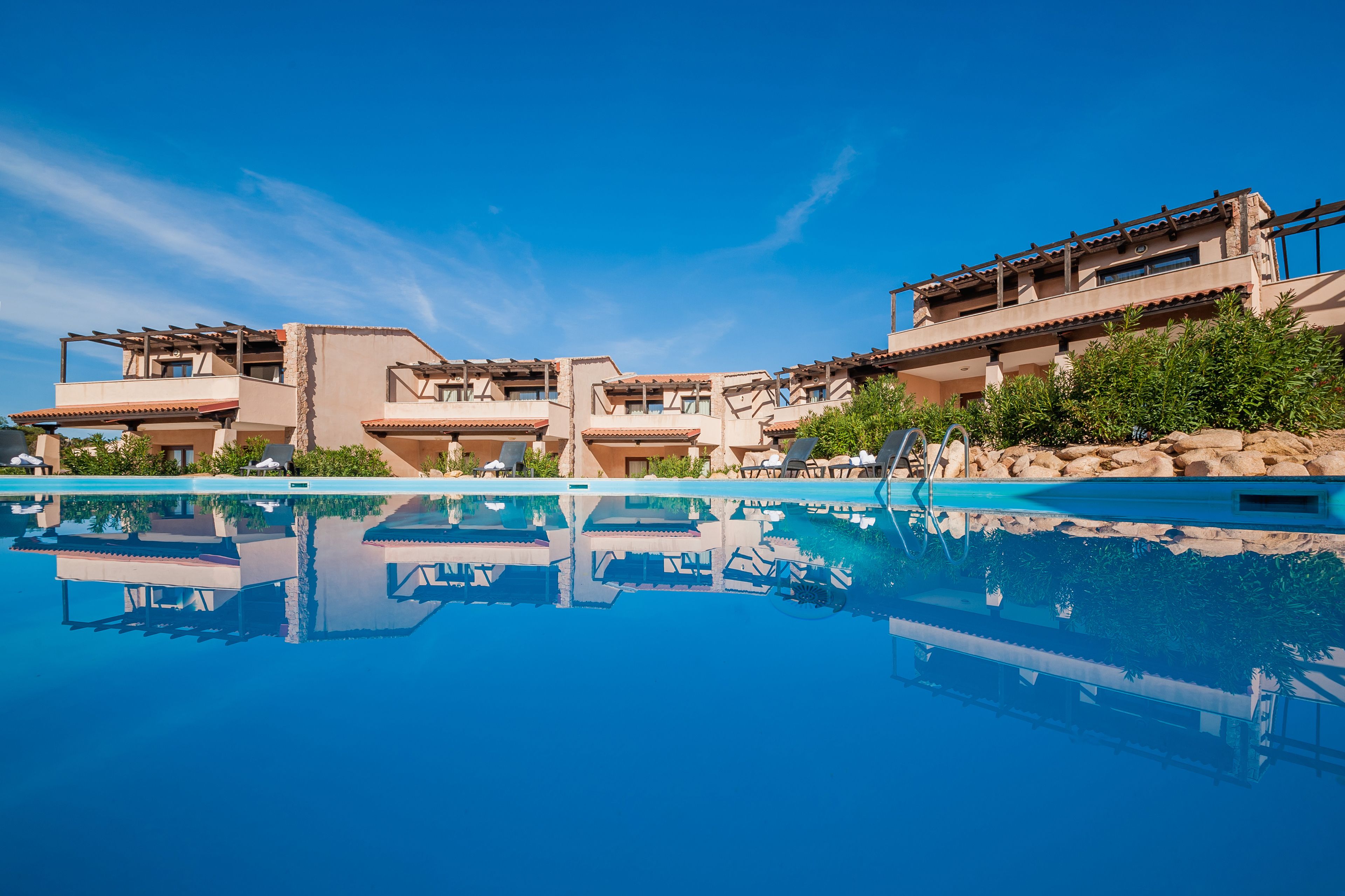 Un resort con piscina cristalina, varias edificaciones con balcones y abundante vegetación.