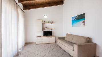 A living room with a beige sofa, a TV on a white cabinet, a painting of a beach, and a wooden ceiling.