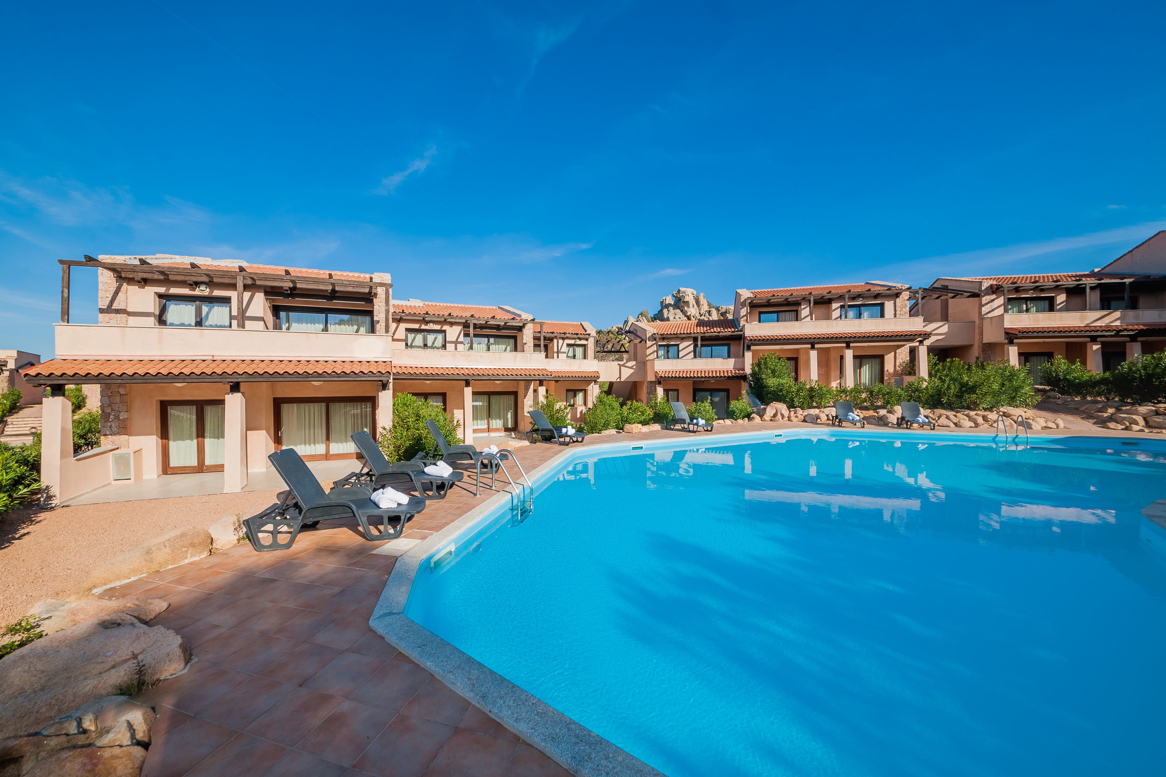 Ein Resort mit Schwimmbad, Liegestühlen und wolkenlosem, blauem Himmel.