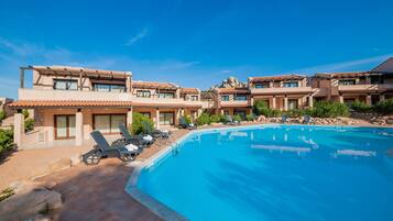 Ein Resort mit Schwimmbad, Liegestühlen und wolkenlosem, blauem Himmel.