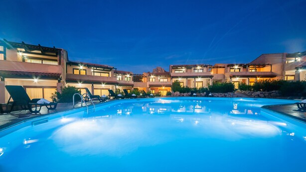 Une piscine avec des chaises longues et, au fond, un bâtiment doté de nombreux balcons.
