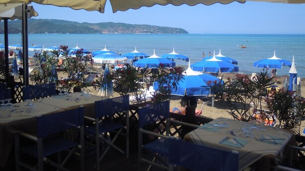 Un restaurant situé en bord de mer, avec une terrasse, des parasols bleus et une vue sur l’océan.