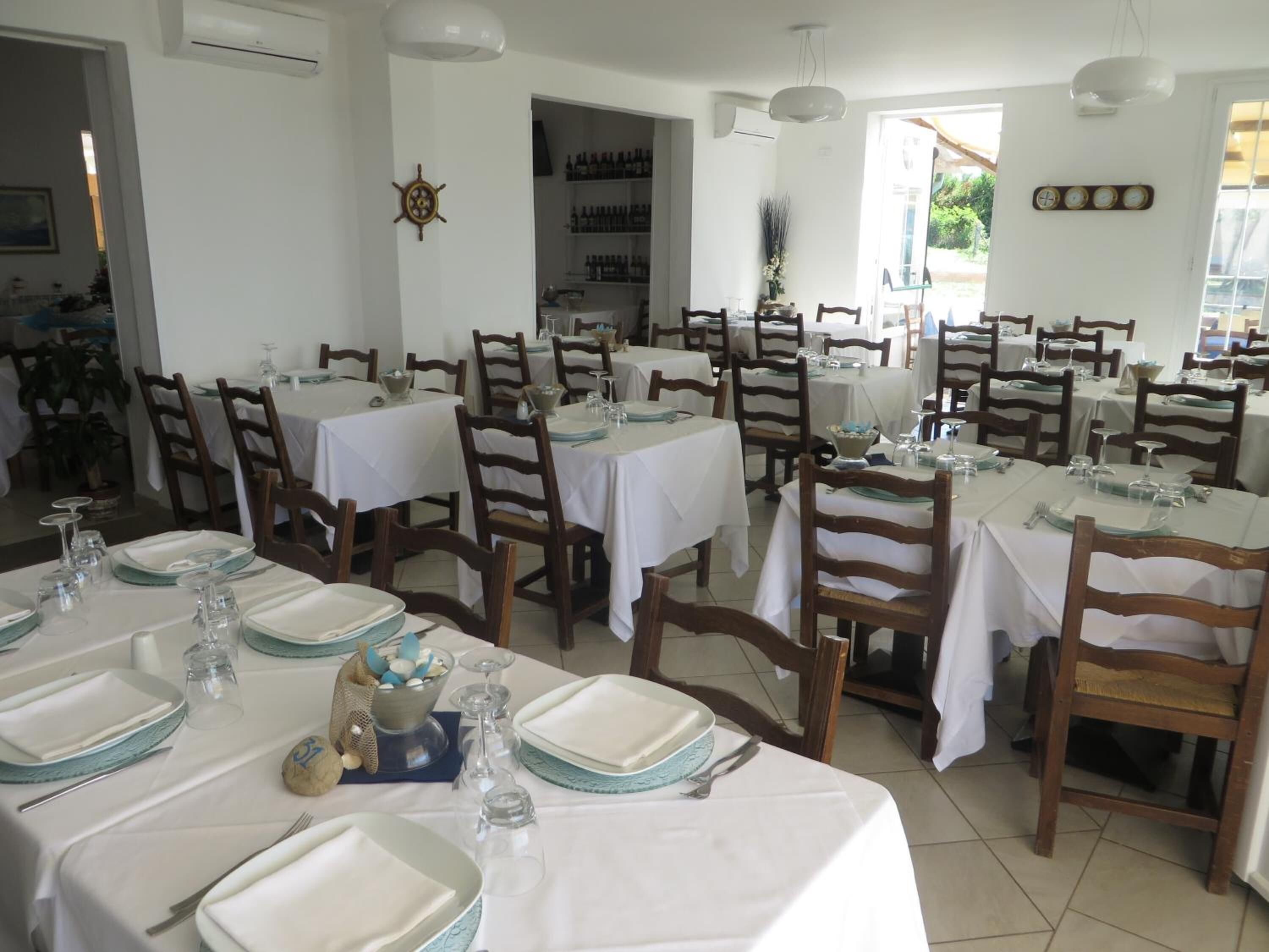 A dining area with multiple tables set for service, wooden chairs, and a white interior.