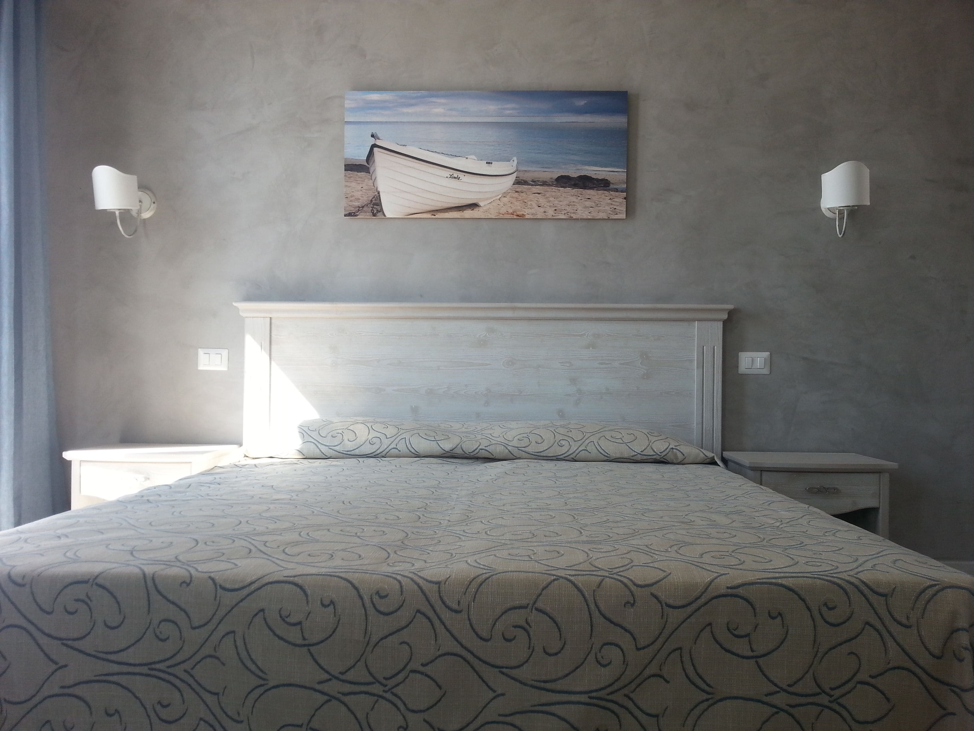 A bedroom with a bed, two bedside tables, and a wall-mounted picture of a boat on a beach.