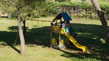 Children can play on the slide and under the shelter in this park playground surrounded by grass and trees.