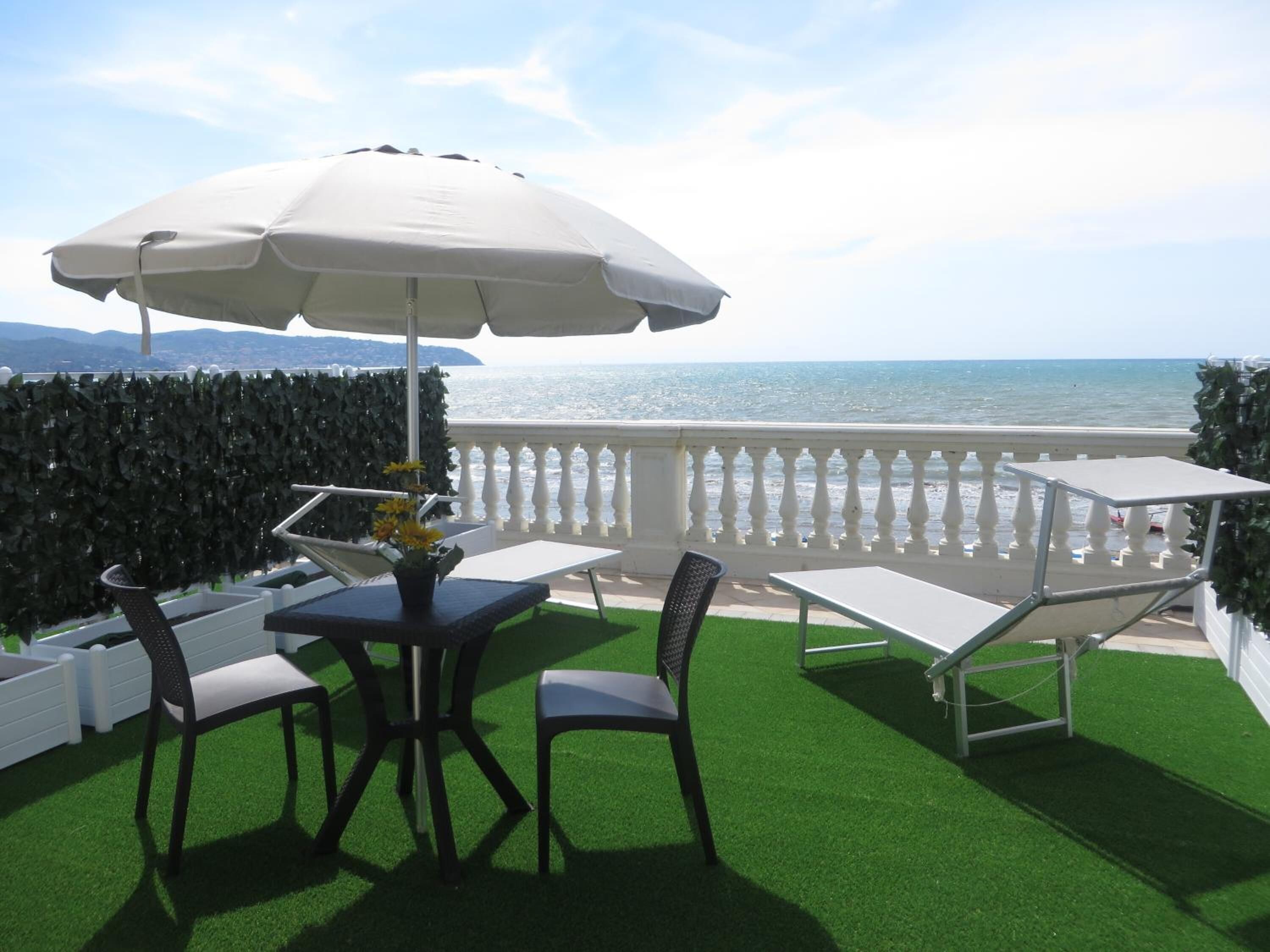 Una terraza con mesa y sillas, un paraguas blanco y vista al mar.