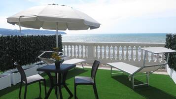 Una terraza con mesa y sillas, un paraguas blanco y vista al mar.